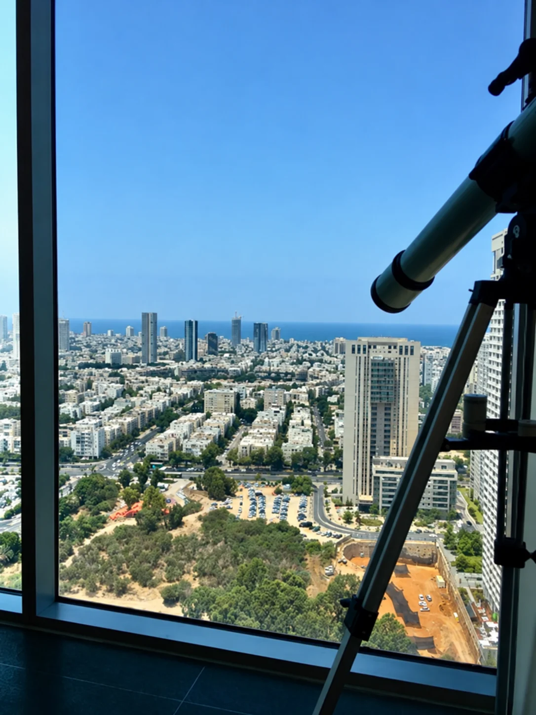 נוף מחלון משרד בקומה גבוהה אל מגדלי תל אביב והים, וטלסקופ ליד החלון