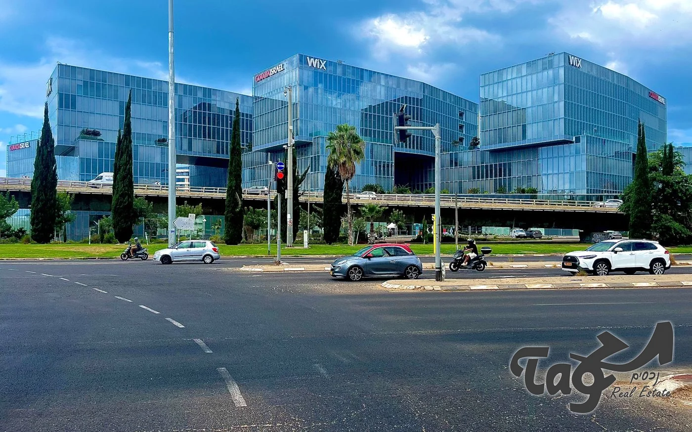 בנייני הזכוכית של המתחם מעבר לכביש רחב, עם ברושים ודקלים