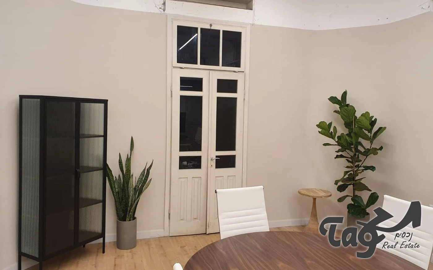 חדר עם קירות בהירים, דלת עץ לבנה גבוהה, עציצים ושולחן ישיבות מעץ