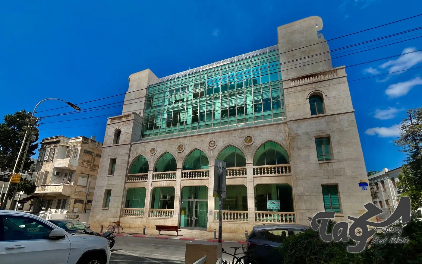 הבניין לשימור מהרחוב: קשתות, מרפסות אבן ותוספת זכוכית ירוקה בקומות העליונות