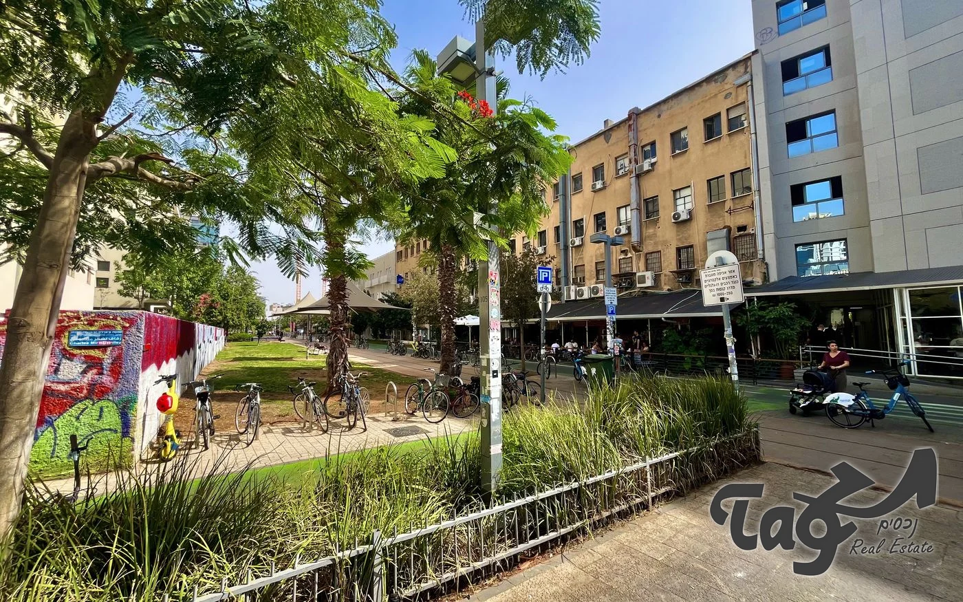 הבניין לצד הבניין הישן הסמוך ופארק המסילה, עם צמחייה, עצים ואופניים חונים