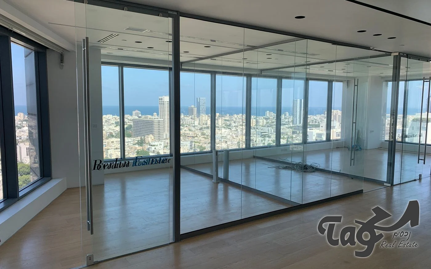 קומת משרדים פנויה עם מחיצות זכוכית, פרקט וחלונות לנוף העיר והים