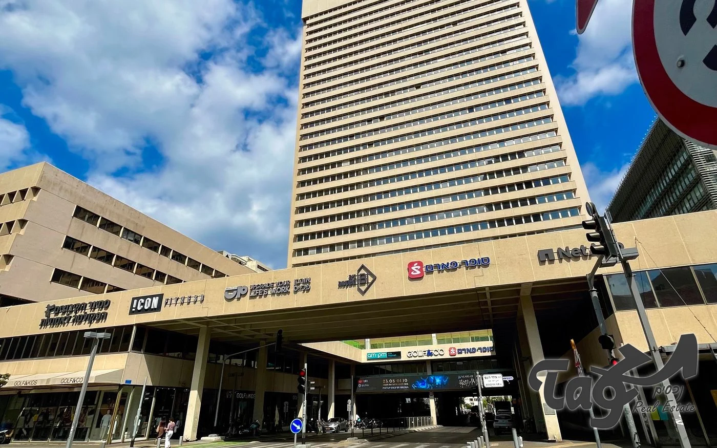 המגדל מעל מבנה מסחרי עם שלטי חנויות ומעבר מקורה לרחוב