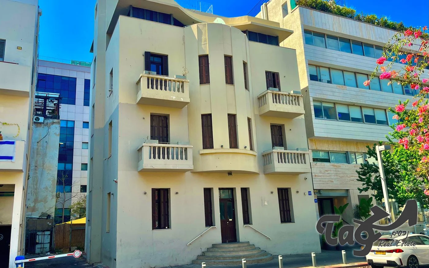 חזית הבניין לשימור: מרפסות, בליטה מעוגלת במרכז, תריסי עץ ומדרגות כניסה