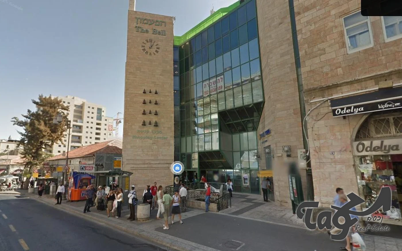 הבניין מהרחוב: מגדל אבן עם שעון בכניסה וחזית זכוכית, ומדרכה הומה אנשים