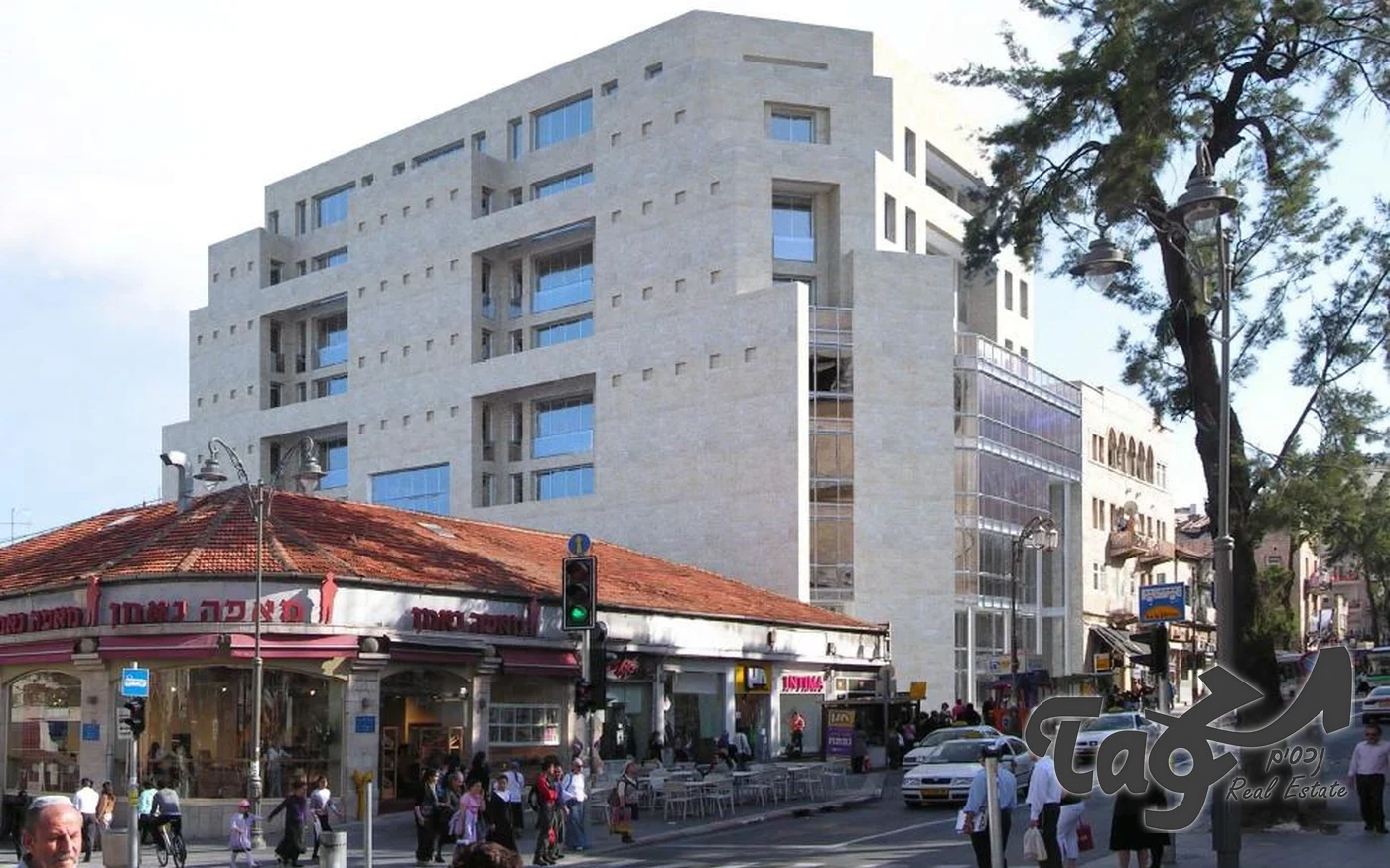 בניין אבן לבן בן כמה קומות מעל מבנה מסחרי ישן בפינת רחוב
