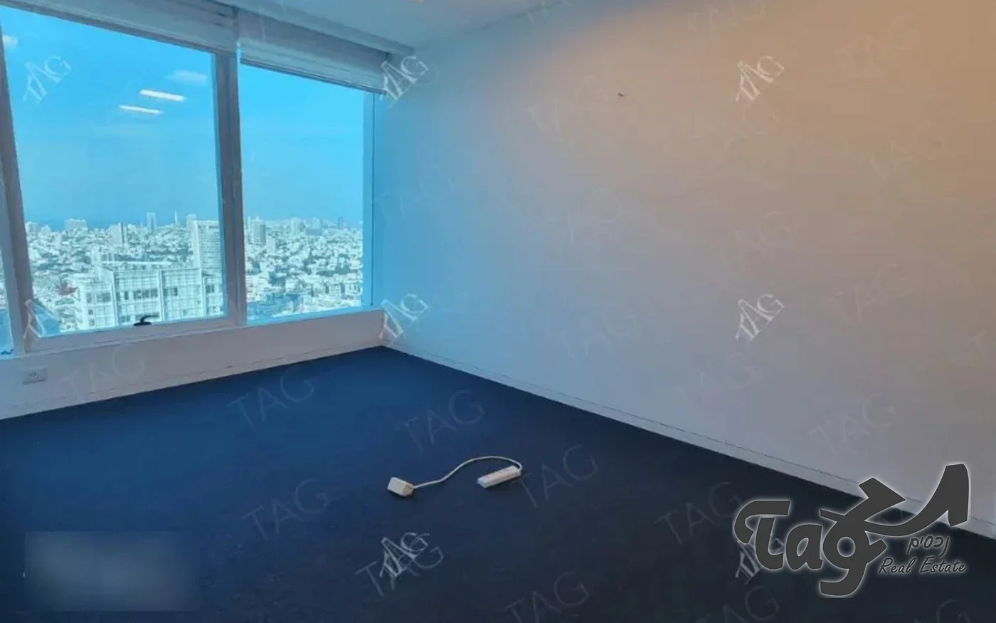 חדר סגור במשרד עם קירות לבנים, שטיח כהה וחלון מול נוף העיר
