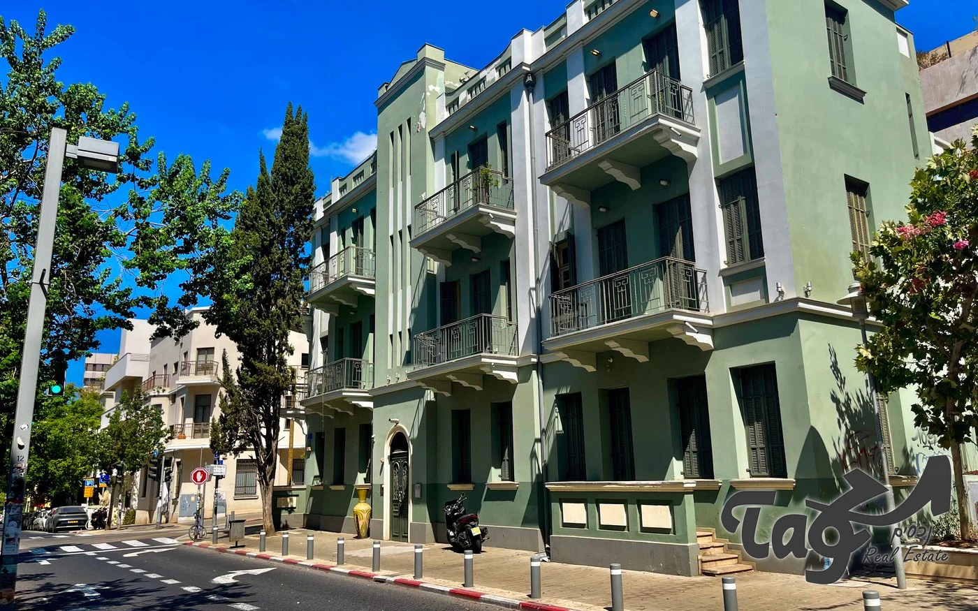 המבנה הירוק לשימור ברחוב יבנה, עם מרפסות בעלות מעקות ברזל ועצים