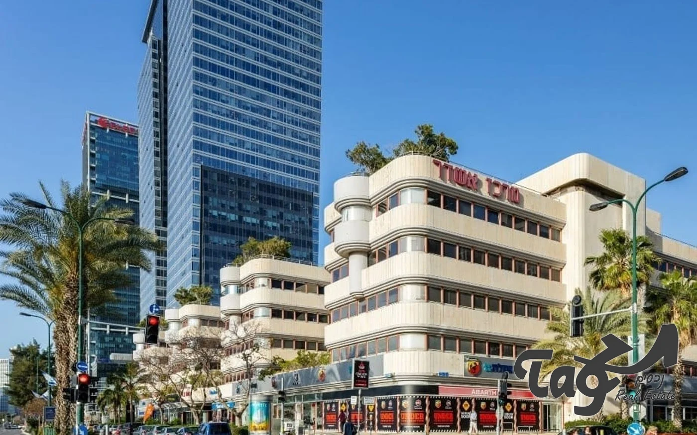 בניין המשרדים ביגאל אלון: חזית בגוון בז׳ עם חלונות סרט ומגדלי משרדים ברקע
